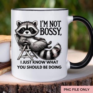 May include: White ceramic mug with a black handle and rim. The mug features a detailed illustration of a raccoon relaxing in a chair, with the text "I'M NOT BOSSY, I JUST KNOW WHAT YOU SHOULD BE DOING."