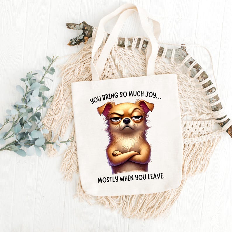 May include: White tote bag with a cartoon dog with a grumpy expression. The text on the bag reads "You bring so much joy... mostly when you leave."