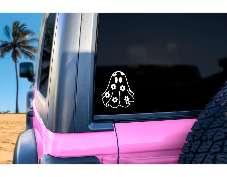 K&ouml;nnte beinhalten: Ein wei&szlig;er Vinyl-Aufkleber mit einem Geist, der ein Blumenmuster tr&auml;gt. Der Aufkleber befindet sich auf der Heckscheibe eines rosafarbenen Jeeps.