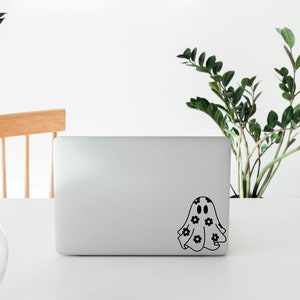 K&ouml;nnte beinhalten: Ein schwarz-wei&szlig;er Geisteraufkleber mit floralem Muster auf einem silbernen Laptop.