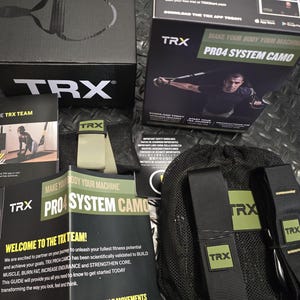 Può includere: Un kit fitness TRX PRO4 SYSTEM CAMO, che include una scatola nera con il logo TRX, materiale didattico e una borsa a rete nera con cinghie. Il kit è progettato per costruire muscoli e aumentare la resistenza.
