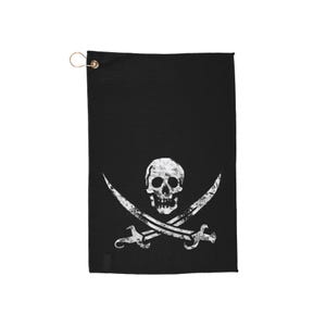 May include: Black golf towel with a white skull and crossbones emblem. The pirate flag design is centrally placed. A gold-coloured grommet is at the top for hanging. The towel is made of a textured material.