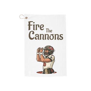 May include: White towel with the text "Fire The Cannons" in brown lettering. The towel features a cartoon illustration of a football player in a helmet and uniform, celebrating with raised arms.