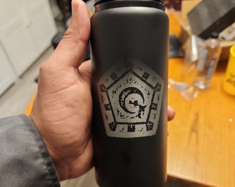 May include: Black insulated water bottle with a black flip-top lid. The bottle features a silver graphic design on the front. The bottle is cylindrical and appears to be made of stainless steel. The bottle is designed to keep beverages cold or hot.