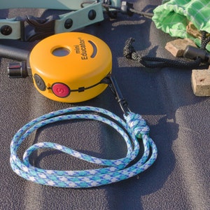 Könnte beinhalten: Ein gelbes Mini-Hundehalsband von Educator mit einem blauen und weißen Seilband. Das Halsband hat einen roten Knopf und einen kleinen Bildschirm. Im Hintergrund befindet sich eine grüne Tasche mit braunen Hunde-Leckerlis.