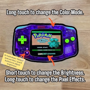 Puede incluir: Una Game Boy Advance SP morada con una carcasa transparente, que muestra el juego Pokemon LeafGreen. La pantalla muestra el t&iacute;tulo del juego y un personaje Pokemon verde. La imagen muestra c&oacute;mo cambiar el modo de color, el brillo y los efectos de p&iacute;xeles en el dispositivo.