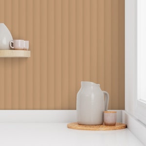 Puede incluir: Una jarra de cerámica blanca y un pequeño tarro de cerámica blanca con tapa de madera se encuentran sobre una bandeja de madera. La bandeja está sobre una encimera blanca frente a una pared con rayas verticales marrones.