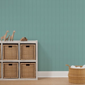 May include: A white shelf unit with six woven baskets, three on each shelf. The shelf unit is against a teal wall with vertical wood paneling. There are three wooden giraffe figurines on top of the shelf unit and a small wooden toy car in front of the shelf unit. A wicker basket with white fabric inside is on the floor to the right of the shelf unit.