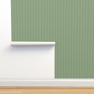 Puede incluir: Un rollo de papel tapiz verde con un patrón de rayas verticales. El papel tapiz está parcialmente desenrollado, revelando una pared blanca detrás.