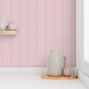 Puede incluir: Una jarra de cerámica blanca y un pequeño tarro de cerámica blanca con tapa de madera se encuentran sobre una bandeja de madera frente a un fondo de panel de madera rosa.