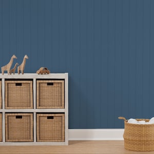 May include: A white wooden shelf unit with six woven baskets. The shelf is against a blue wall with white trim. A toy car and three wooden giraffe figurines are on top of the shelf. A wicker basket with white fabric inside is on the floor.