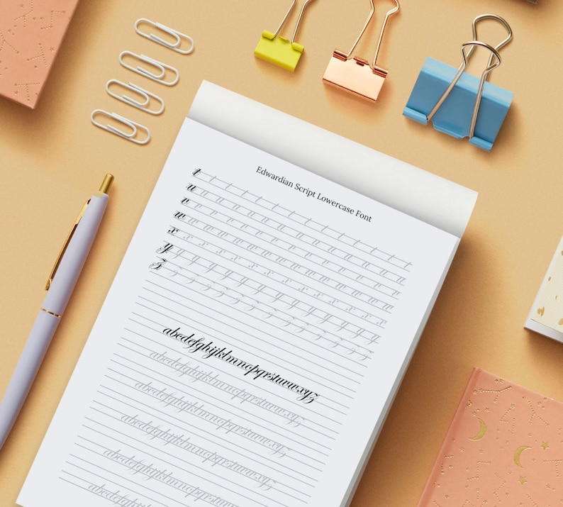 May include: A white notebook with lined paper and the text "Edwardian Script Lowercase Font" at the top. The notebook has several lines of lowercase letters written in cursive, including the alphabet and the word "abcdefghijklmnopqrstuvwxyz".