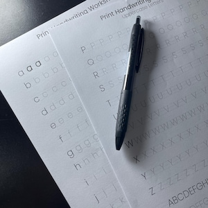 May include: A black pen lies on top of a white sheet of paper with a handwriting worksheet. The worksheet has lines for practicing writing uppercase letters in English. The letters are printed in a light grey colour.