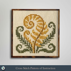 Può includere: Un ricamo a punto croce quadrato con un motivo centrale a forma di fronda di felce giallo oro, affiancato da due fronde di felce verde scuro più piccole, cucito su tessuto Aida color crema e incorniciato in una cornice quadrata in legno.