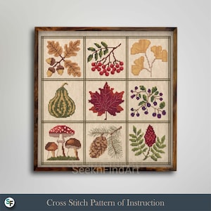 May include: A framed cross stitch sampler featuring a grid of nine squares, each displaying a different botanical element including oak leaves with acorns, red berries, ginkgo leaves, a gourd, a maple leaf, dark berries, mushrooms, a pinecone, and a sumac branch.