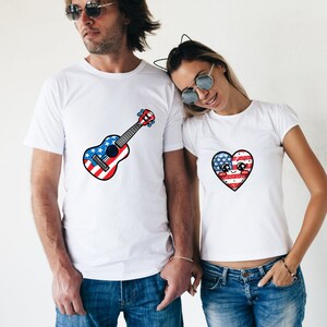 May include: A couple wearing white t-shirts with a patriotic theme. The man's shirt features a ukulele with an American flag design. The woman's shirt features a heart with an American flag design.