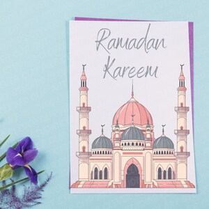 May include: A white card with a purple border features a cartoon illustration of a mosque with the text "Ramadan Kareem" in gray lettering.