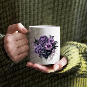 May include: White ceramic mug with a black and purple floral design. The flowers are arranged around a skull with dripping paint.