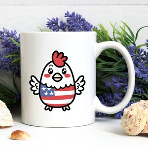May include: White ceramic mug with a cartoon chicken wearing an American flag design. The chicken has red comb and wattle, black eyes, and a yellow beak.