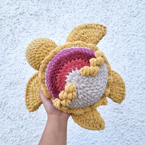 May include: A crocheted stuffed turtle toy with a yellow and brown shell and a pink and red centre. The turtle is made with soft yarn and has a whimsical design.