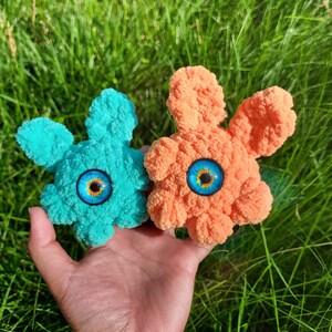 Peut inclure: Deux jouets en peluche crochetés avec des yeux globuleux. L'un est bleu et l'autre est orange.