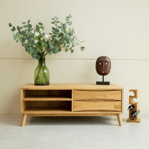 Peut inclure: Un meuble TV en bois clair avec deux tiroirs et une étagère. Le meuble est décoré d'un masque en bois sculpté et d'un porte-bouteilles en bois avec trois bouteilles de vin.