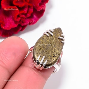 May include: A teardrop-shaped ring featuring a textured, metallic bronze-gold stone set in a polished silver band with prong settings. The stone displays a mottled, granular surface pattern. The text RhythmOfJewels is visible on the image.