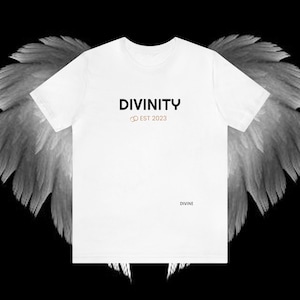 Könnte beinhalten: Weißes T-Shirt mit dem Text "DIVINITY" in Schwarz und "EST 2023" in Gold. Das Wort "DIVINE" ist in kleinen Buchstaben unten auf dem Shirt gedruckt.
