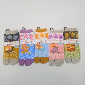 May include: Five pairs of Japanese tabi socks with various patterns and colors. Each pair features a split toe design and a tag. The patterns include fish, waves, and other traditional Japanese motifs. The socks have a gray cuff and a colorful foot.
