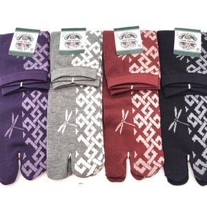 Puede incluir: Cuatro pares de calcetines Tabi en morado, gris, burdeos y negro. Cada calcetín presenta un patrón geométrico blanco y un diseño de libélula. Los calcetines tienen un diseño de puntera dividida y una etiqueta que dice "Made in Japan".