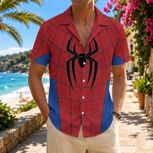 K&ouml;nnte beinhalten: Rotes kurz&auml;rmeliges Hemd mit einem Spider-Man-Netzdesign und einem gro&szlig;en schwarzen Spinnenemblem. Das Hemd hat blaue Akzente an den &Auml;rmeln und Seiten. Knopfleiste.