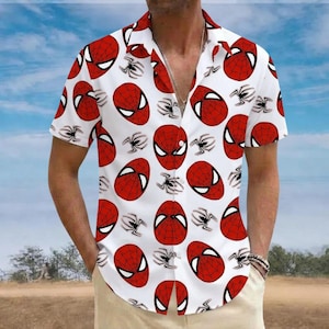 May include: White short-sleeve button-down shirt featuring a repeating pattern of red Spider-Man mask designs and black spider silhouettes. The shirt has a classic collar and is worn open. The background shows a blue sky and a field.