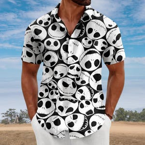 Puede incluir: Una camisa de manga corta con botones y un estampado integral de varios rostros de calaveras de Jack Skellington en blanco y negro. La camisa tiene un cuello clásico, una tapeta de botones frontal y un patrón repetitivo de cabezas esqueléticas.