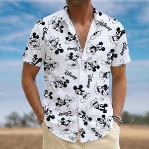 Può includere: Una camicia bianca a maniche corte con abbottonatura frontale, caratterizzata da una stampa a linee nere di Topolino in varie pose e dalla scritta Disney in corsivo. La camicia presenta un colletto classico e un orlo dritto.