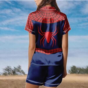 May include: Navy blue Spider-Man themed pajama set. The top features a red spiderweb design on the shoulders and a large red spider emblem on the back. The shorts and top have white trim.