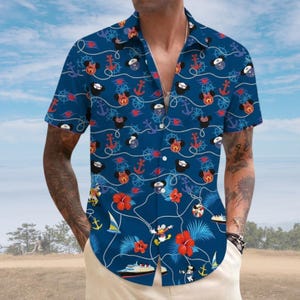 Op de afbeelding: Een donkerblauw overhemd met korte mouwen en knoopsluiting, voorzien van een nautisch patroon. De print bevat Mickey en Minnie Mouse iconen, rode ankers, scheepssturen, zeilboten, cruiseschepen en felrode hibiscusbloemen.