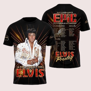 May include: A black short-sleeve t-shirt featuring a graphic of Elvis Presley in a white jumpsuit on the front with the text THE KING OF ROCK 'N' ROLL ELVIS. The back displays a concert tour schedule with the text BAZ LUHRMANN'S EPIC ELVIS PRESLEY.