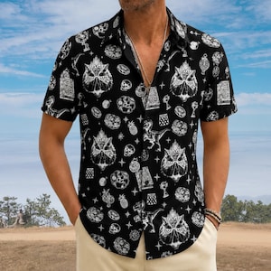 May include: A black short-sleeved button-down shirt featuring a white repeating pattern of owl faces, dinosaur silhouettes, treasure chests, skulls, pineapples, and star shapes. The shirt has a classic collar and a buttoned front placket.