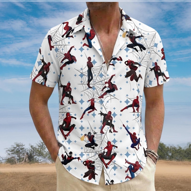May include: White short-sleeve button-down shirt featuring a repeating pattern of Spider-Man figures, spiderwebs, and blue diamond shapes. The shirt has a classic collar and is worn open. The background shows a blue sky and a field.
