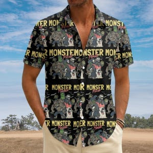 May include: A black short-sleeved button-down shirt featuring a repeating pattern of cartoon monsters and ghosts. The text "MONSTER MASH" is printed in yellow capital letters across the fabric, interspersed with various colorful monster illustrations.