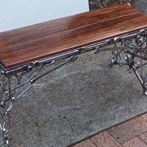 Op de afbeelding: Een houten bank met een uniek metalen frame gemaakt van moersleutels en andere gereedschappen. De bank is gemaakt van donker hout en heeft een rustieke uitstraling.