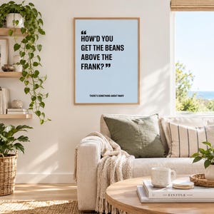 May include: A rectangular wall art print in a light wood frame featuring a light blue background with black text that reads, "HOW'D YOU GET THE BEANS ABOVE THE FRANK?" and below that, "THERE'S SOMETHING ABOUT MARY" in a smaller, sans-serif font.