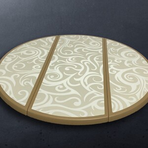 Op de afbeelding: Een ronde, beige onderzetter met een decoratief, wervelend wit patroon. De onderzetter is verdeeld in drie secties en heeft een bruine rand. Dit keukenaccessoire beschermt oppervlakken tegen hete gerechten.