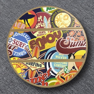 Op de afbeelding: Ronde houten serveerschaal met een collage van surf-thema stickers. Het ontwerp bevat tekst als "Enjoy Summer", "Surf" en "Honolulu". De schaal heeft een bruine rand en is verdeeld in secties.