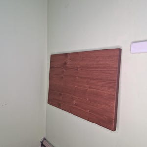 Könnte beinhalten: Ein brauner, klappbarer Holztisch, der an einer Wand montiert ist. Der Tisch befindet sich in einer Ecke eines Raumes mit weißen Wänden und weißen Leisten.