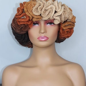May include: A crocheted hat with a unique design featuring multiple layers of brown, tan, and beige crocheted flowers. The hat is worn on a mannequin head.