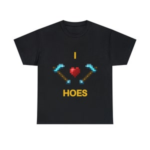 Könnte beinhalten: Schwarzes T-Shirt mit einem Pixel-Design aus zwei gekreuzten Spitzhacken und einem roten Herzen. Der Text "I ♥ HOES" ist in Gelb unter dem Design geschrieben.