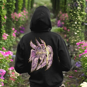 Puede incluir: Sudadera con capucha negra con un estampado gráfico de un ángel morado y dorado con las alas extendidas. El ángel sostiene un orbe brillante en sus manos.