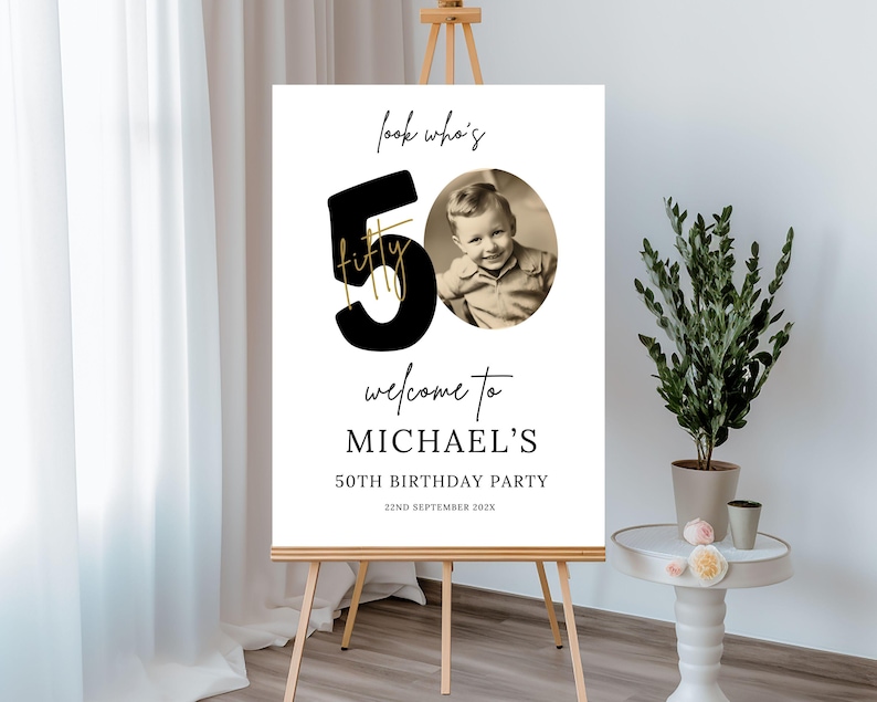 May include: A black and white welcome sign for a 50th birthday party. The sign features a large black number 50 with the word "fifty" written in gold script. The sign also includes a photo of a young boy and the text "Look who's welcome to Michael's 50th Birthday Party 22nd September 2023".