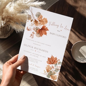 Puede incluir: Una tarjeta de invitación rectangular blanca para baby shower con ilustraciones en acuarela de hojas de otoño en tonos naranja, marrón y verde suave. El texto dice Falling In Love with Baby Clifford y honra a Olivia Richards.